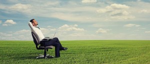 Image of a man sitting on a chair in a field with a laptop on his lap